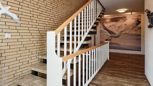 A staircase with a wooden handrail and white balusters, leading to a landing with a mural of birds. - Ferienwohnung Balkon zur Sonnenseite in Bensersiel (Bensersiel)