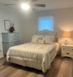 A bedroom with a bed, a nightstand, a dresser, a ceiling fan, and a window with curtains.