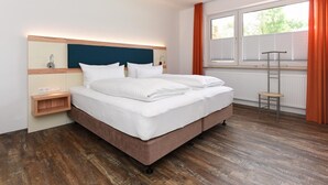 Et moderne hotelværelse med en stor seng, et natbord, et vindue med persienner og trægulv.