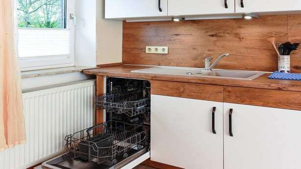 A kitchen with white cabinets, a wooden countertop, a dishwasher, and a window with a view of trees. - Ferienwohnung in Bensersiel (Bensersiel)