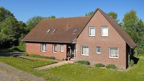A two-story brick house with a sloped roof, a front porch, and a small garden area. - Ferienwohnung in Bensersiel (Bensersiel)