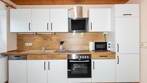 A compact kitchen with white cabinets, a stainless steel range hood, a microwave, and an oven. - Ferienwohnung in Bensersiel (Bensersiel)