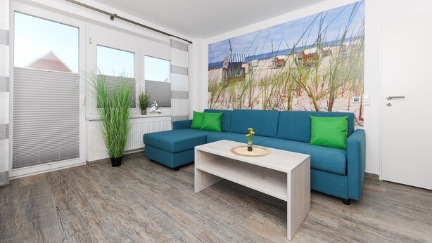 A modern living room with a blue sofa, green cushions, a wooden coffee table, and a beach-themed mural on the wall.