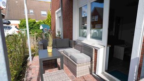 A small patio with wicker furniture, a table, and a door leading to a room.