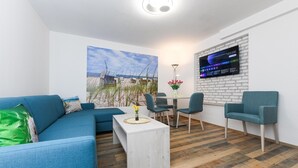 Uma sala de estar moderna com um sofá azul, uma mesa de centro branca e um espaço de jantar com cadeiras e uma mesa.