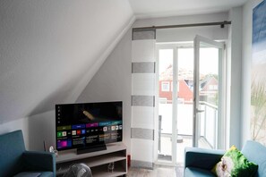 Una sala de estar con televisor de pantalla plana, un sofá y un ventanal corredera que da a un espacio exterior.