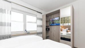 Quarto de hotel com duas camas, uma televisão e uma janela com cortinas.