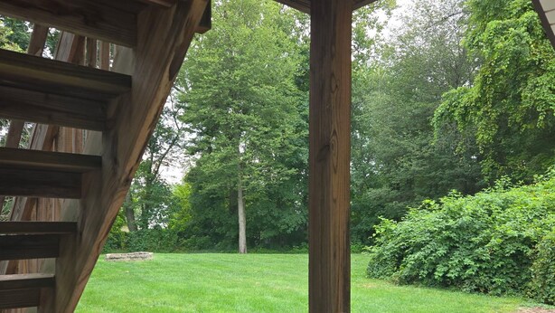 Un patio couvert avec vue sur une pelouse verdoyante et un trampoline.