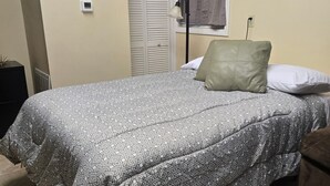 Une chambre à coucher avec une couvre-lit à motifs, une lampe de chevet, une fenêtre avec des rideaux et un radiateur.