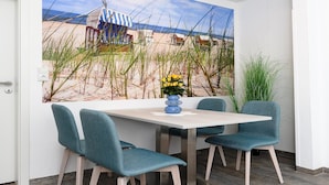 En matplats med utsikt över stranden, ett bord, fyra turkosa stolar och en vas med gula blommor.
