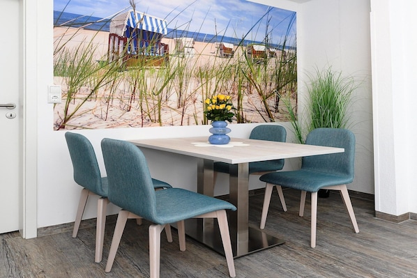 A dining area with a beach view, a table, four teal chairs, and a vase with yellow flowers.