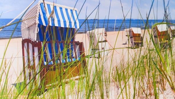 En strand med ett randigt strandparasoll och solstolar.