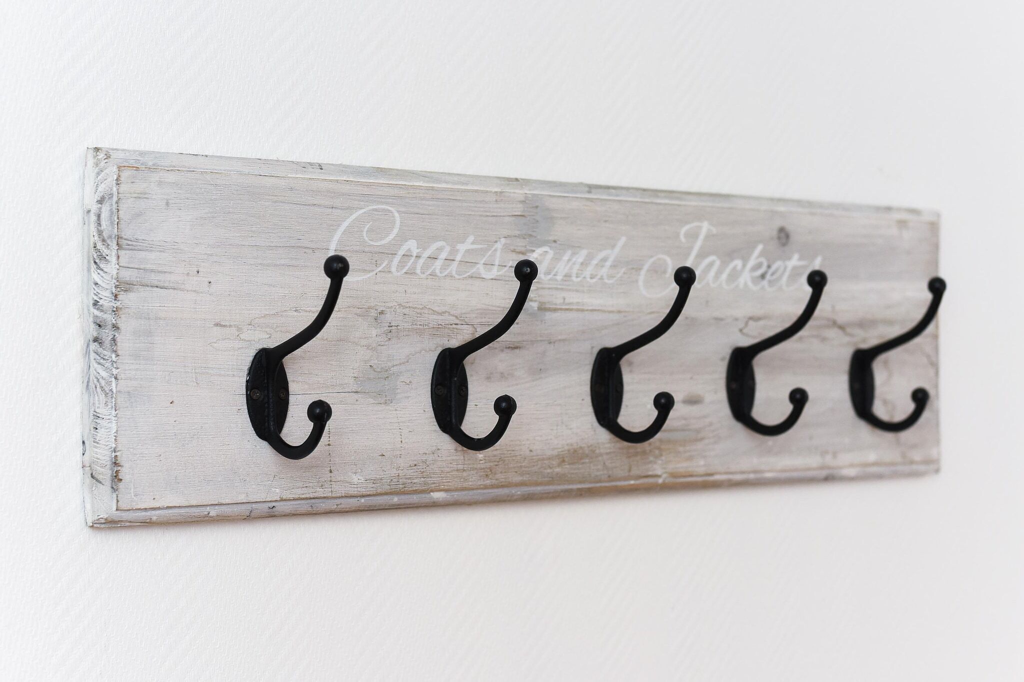 A rustic wooden wall-mounted coat rack with four hooks and the words "Coats and Jacket" written on it.