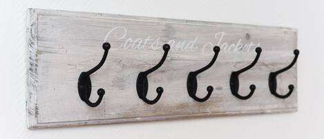 A rustic wooden wall-mounted coat rack with four hooks and the words "Coats and Jacket" written on it.