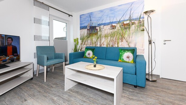 Un salon moderne avec un canapé bleu, une table basse blanche et un tableau représentant une scène de plage.