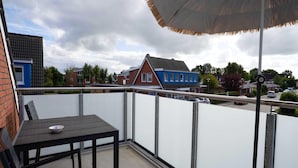 Un balcon avec une table et des chaises, une vue sur des immeubles d’habitation et une rue où circulent des voitures.