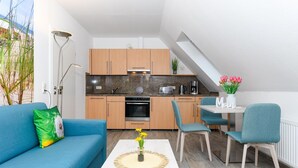 Une cuisine compacte dotée d’appareils électroménagers modernes, un coin repas avec une table et des chaises, et un espace de vie avec un canapé et un coussin décoratif.