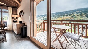 A wooden deck with a table and chairs, a view of a valley, and a wooden interior with a desk and lamp. - Ardelle - alpine duplex with hot tub, Les Gets (Les Gets)