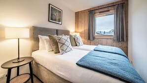 A bedroom with a bed, a bedside table, a lamp, a window with curtains, and a framed picture on the wall. - Ardelle - alpine duplex with hot tub, Les Gets (Les Gets)