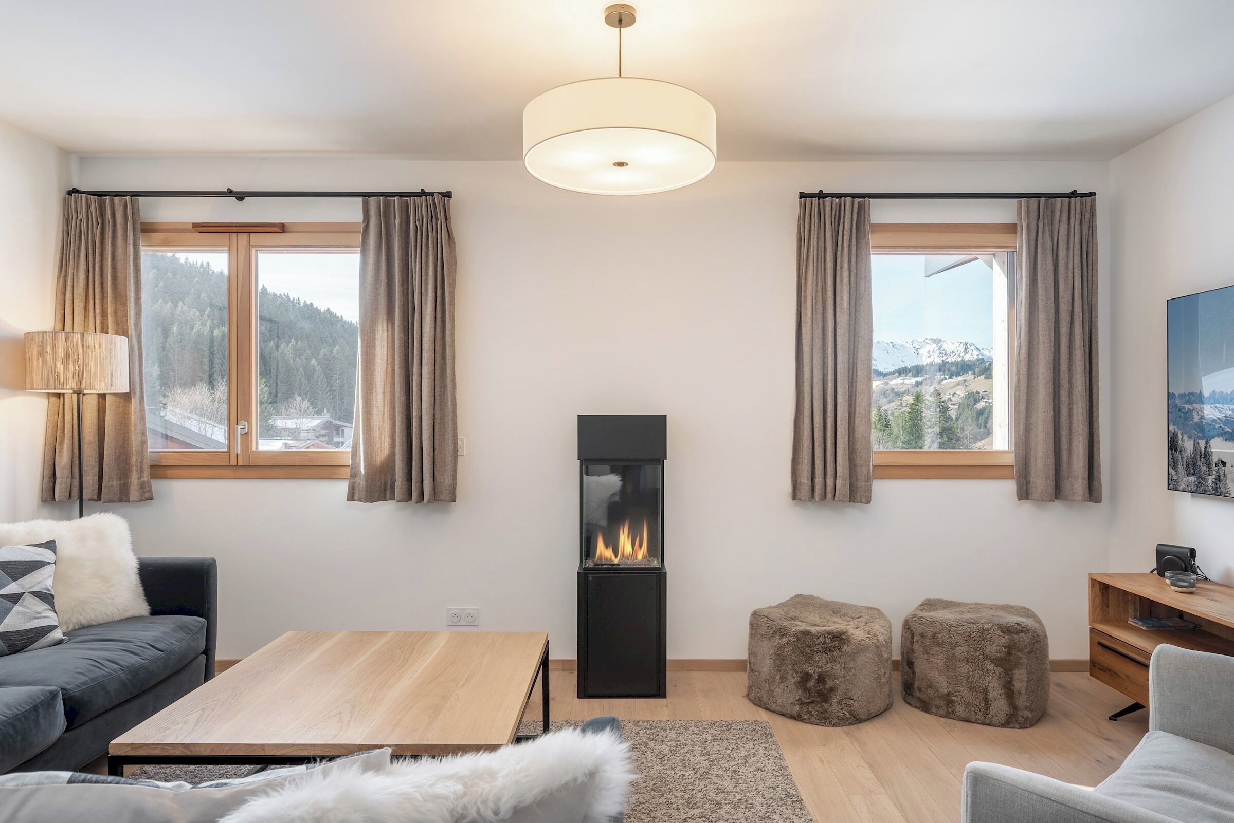 A modern living room with a fireplace, a sofa, a coffee table, and a view of a snowy mountain landscape.