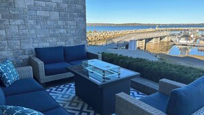 Eine Terrasse mit Korbmöbeln, einem Tisch mit Glasplatte und Blick auf Boote und Wasser.