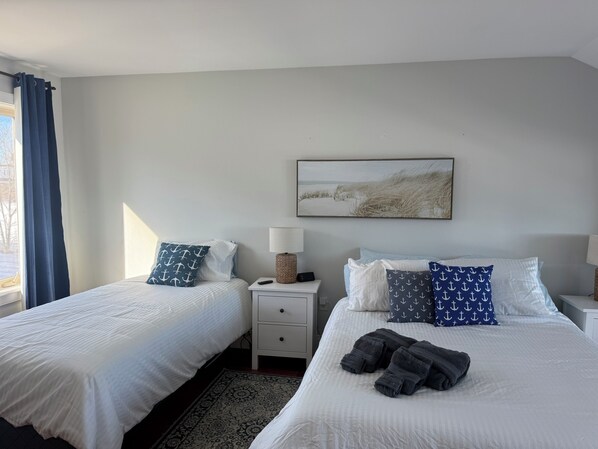 A hotel room with two beds, a nightstand with a lamp, a rug, and a beach-themed painting on the wall.