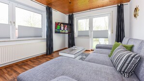 A modern living room with a grey sofa, a coffee table, and a painting on the wall. - Geräumige Ferienwohnung mit Terrasse in Bensersiel (Bensersiel)