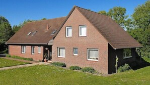 A two-story brick house with a sloped roof, multiple windows, and a small porch. - Geräumige Ferienwohnung mit Terrasse in Bensersiel (Bensersiel)