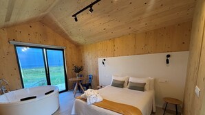A modern bedroom with a large bed, a bathtub, and a view of the outdoors. - Cabañas Camiño do Mar  (Foz)