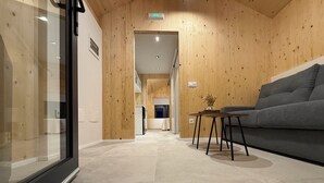 A modern interior with wooden panel walls, a grey sofa, a small table, and a glass door. - Cabañas Camiño do Mar  (Foz)