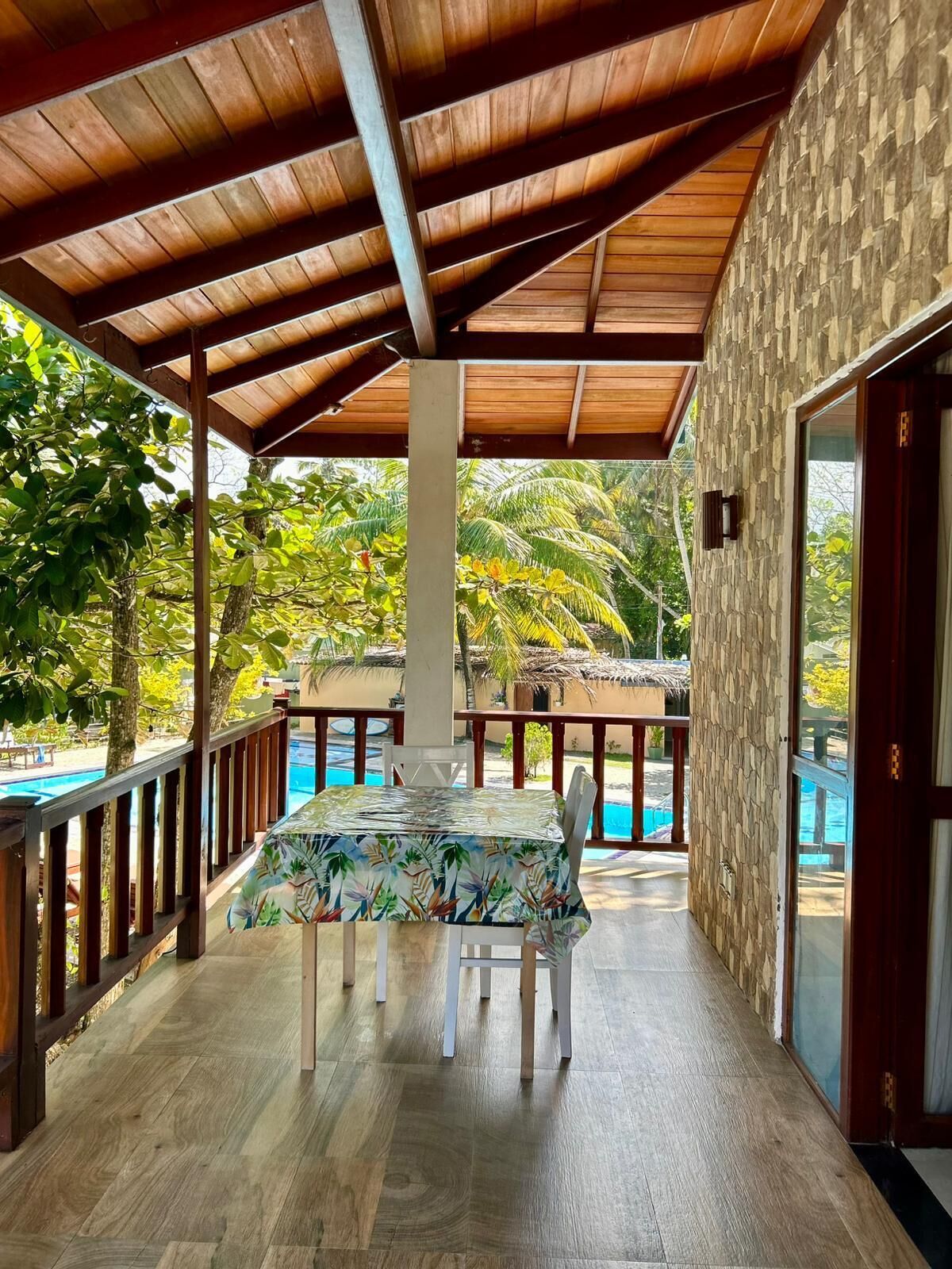 A covered outdoor area with a pool, wooden deck, and a table with a floral tablecloth.