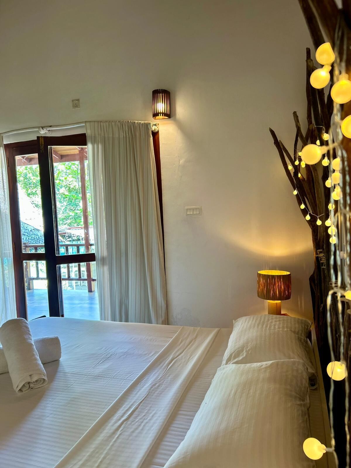 A hotel room with a bed, a chair, a lamp, and a view of the outdoors.