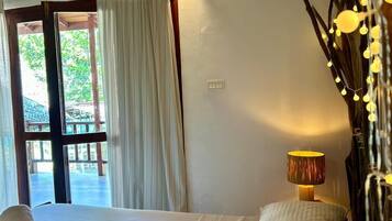 A hotel room with a bed, a chair, a lamp, and a view of the outdoors.