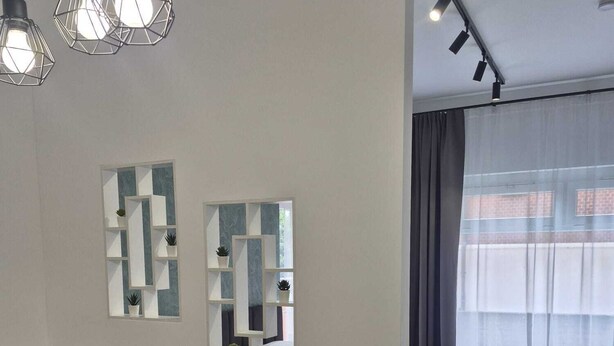 Un espace de salle à manger moderne avec une table en bois, des chaises noires et des luminaires suspendus. On y trouve deux miroirs fixés au mur et une fenêtre avec des rideaux.