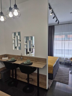 Ein moderner Essbereich mit Holztisch, schwarzen Stühlen und Pendelleuchten. Zwei Wandspiegel und ein Fenster mit Vorhängen sind vorhanden.