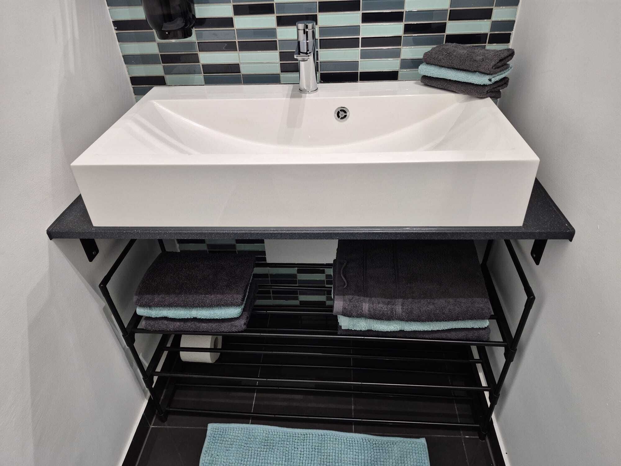 A bathroom with a white sink, black towel rack, and a tiled backsplash.