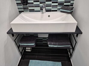 Ein Badezimmer mit einem weißen Waschbecken, einem schwarzen Handtuchhalter und einer gefliesten Rückwand.