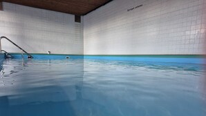 Une piscine intérieure à l’eau claire, avec un escalier en métal et des murs carrelés.