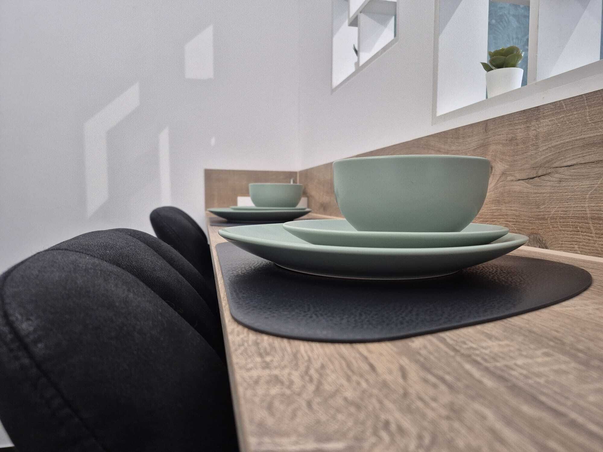 Un comedor moderno con una mesa de madera y un cojín negro. Hay dos cuencos verdes y un plato a juego sobre la mesa.