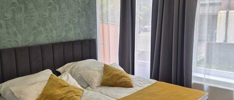 A bedroom with a bed, a green textured wall, and a window with curtains.