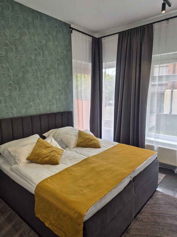 Ein Schlafzimmer mit einem Bett, einer Wand mit Grüner Textur und einem Fenster mit Vorhängen.