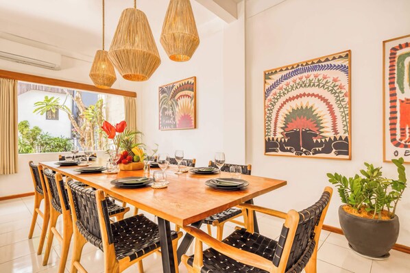 Comedor con mesa de madera, sillas con acolchado negro y lámparas colgantes tejidas.