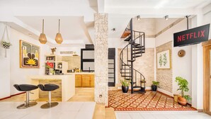 Un interior moderno con cocina, comedor y una escalera que sube a un altillo. Se ve un cartel de Netflix.