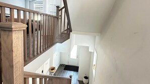 Un escalier en bois mène à un deuxième étage, et on aperçoit à l’arrière-plan un espace cuisine.