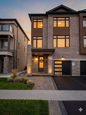 A two-story residential building with a garage, a front entrance with a door, and a small garden area.