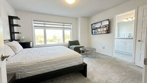 Une chambre à coucher comprenant un lit, une chaise, une petite table, un téléviseur, et une salle de bain avec un miroir et des placards.