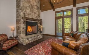 Una sala de estar con chimenea de piedra, sofá de cuero y un ventanal grande.