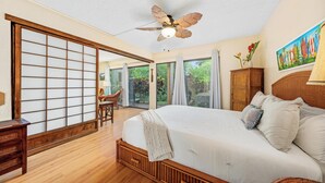 Een slaapkamer met een groot bed, een plafondventilator, een shoji-scherm, uitzicht op de omgeving en een schilderij aan de muur.