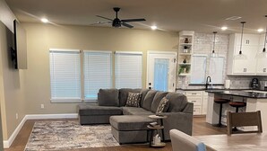 A spacious living area with a sectional sofa, a dining table with chairs, and a kitchen area with white cabinets and pendant lights.