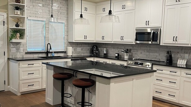 A modern kitchen with white cabinets, a central island with stools, a microwave, and a coffee maker.